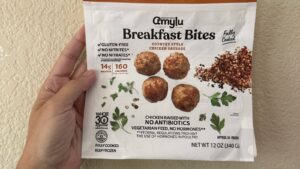 A hand holding a package of frozen chicken sausage bites covered in gluten-free and Whole30 label claims.