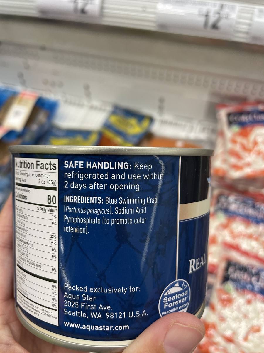 A can of crab meat held up in a grocery store showing a two-item ingredient list.