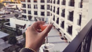 Cocktail held over the private terrace railing at The Global Ambassador hotel in Phoenix, Arizona, at sunset, overlooking the courtyard and stone facade
