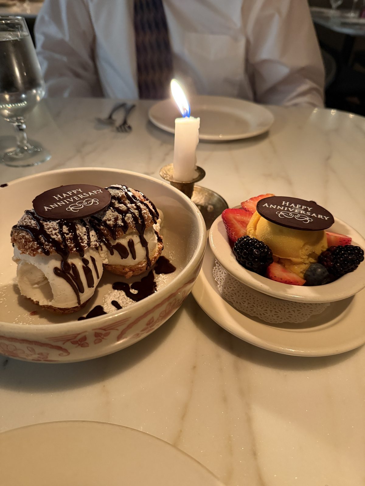 Two anniversary desserts at Le Ame, a profiterole and a gluten free dairy free mango sorbet with berries, each topped with a Happy Anniversary chocolate medallion