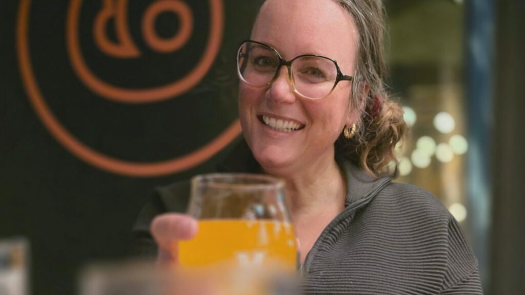 Nichole Holze raising a glass of gluten free beer in a restaurant, smiling at the camera