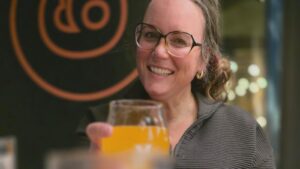Nichole Holze raising a glass of gluten free beer in a restaurant, smiling at the camera